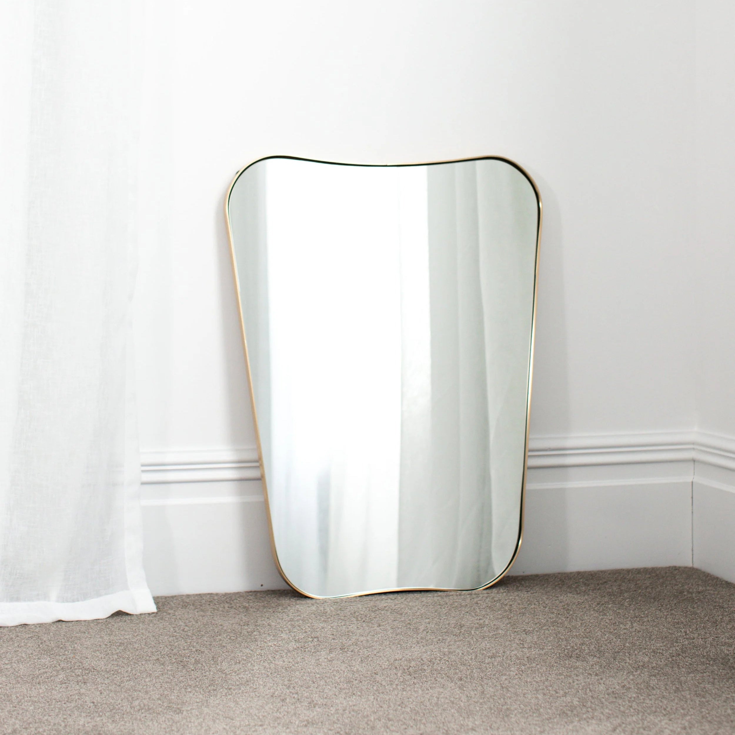 Rectangular mirror with gold frame on a white wall and gray carpet