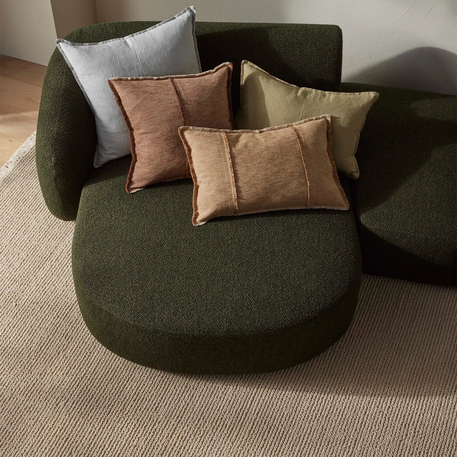 Green sofa with cushions on a neutral background and stone woven rug