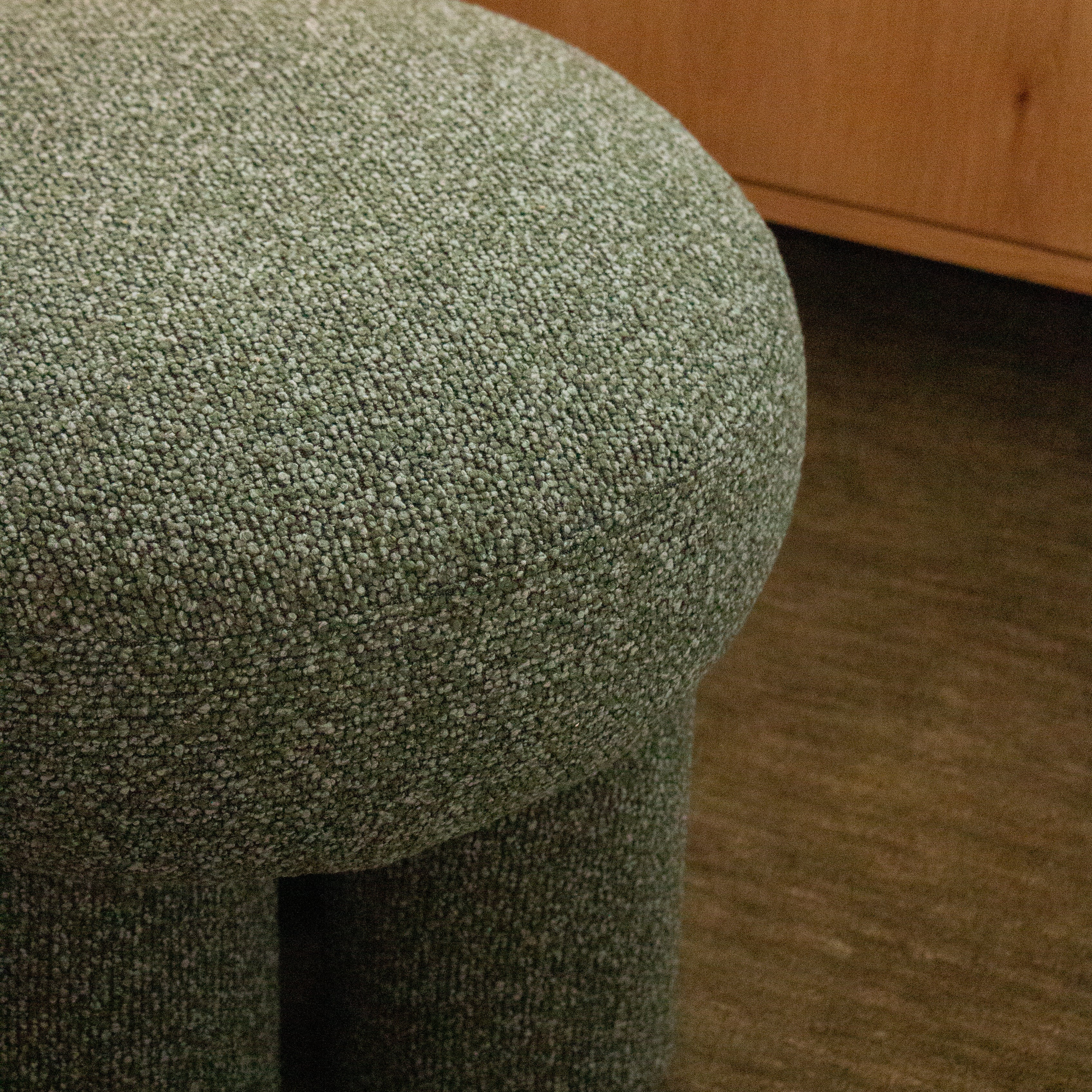 Close-up of a textured green stool on a wooden floor.