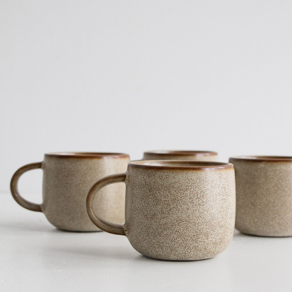 Set of four ceramic mugs with a speckled texture on a light background