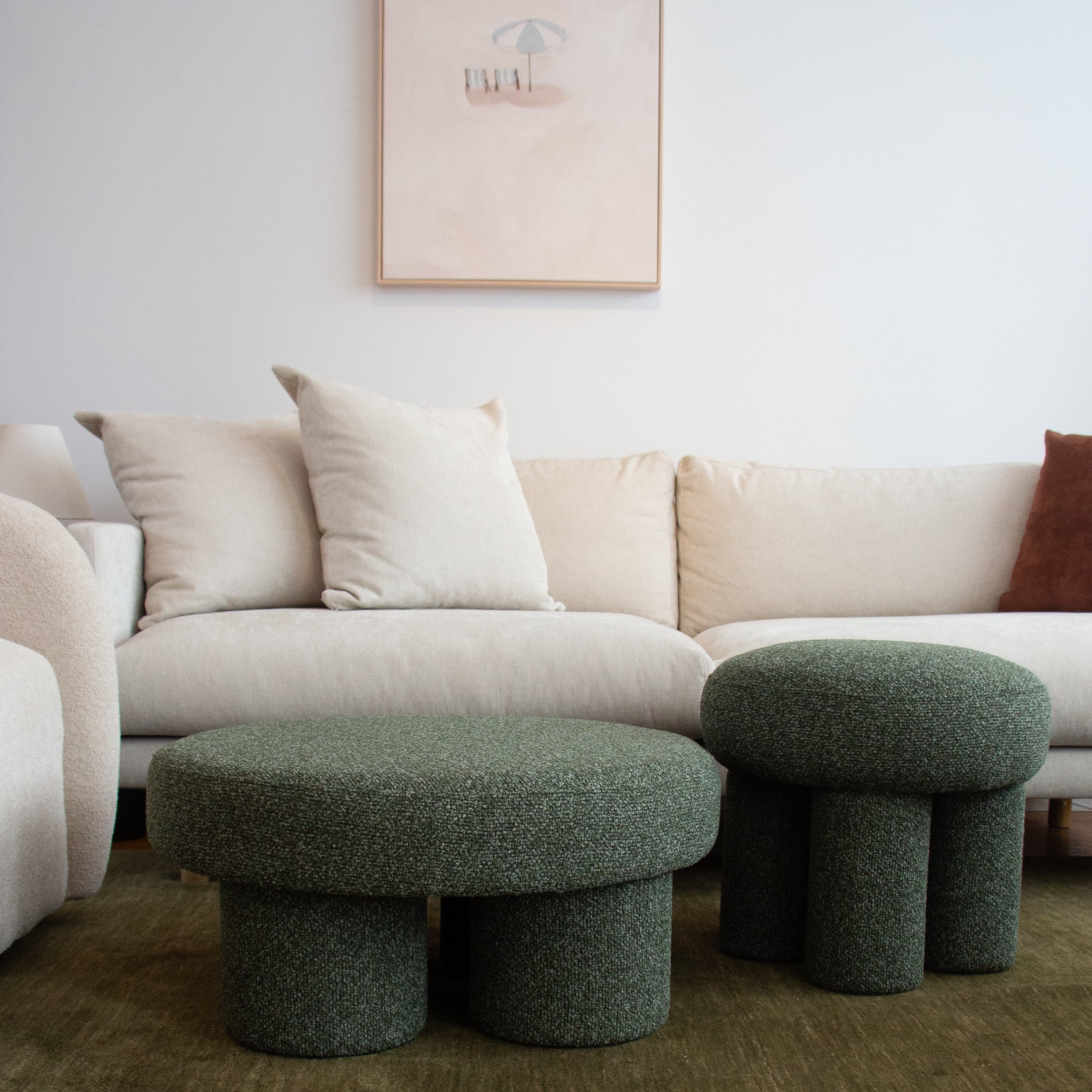Beige sectional sofa with decorative pillows and two green ottomans in a living room setting.