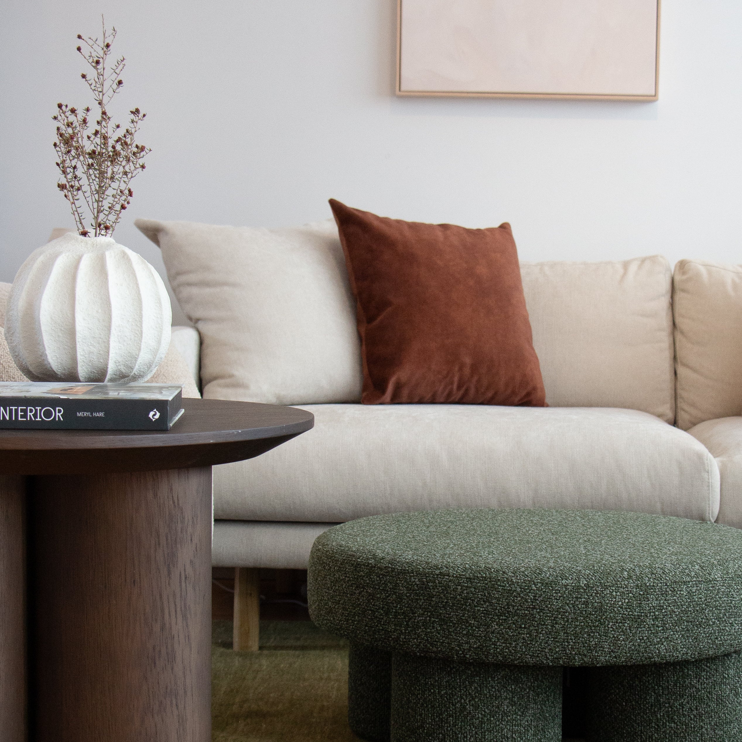 Beige sofa with a brown pillow, green ottoman, and wooden side table in a living room setting.