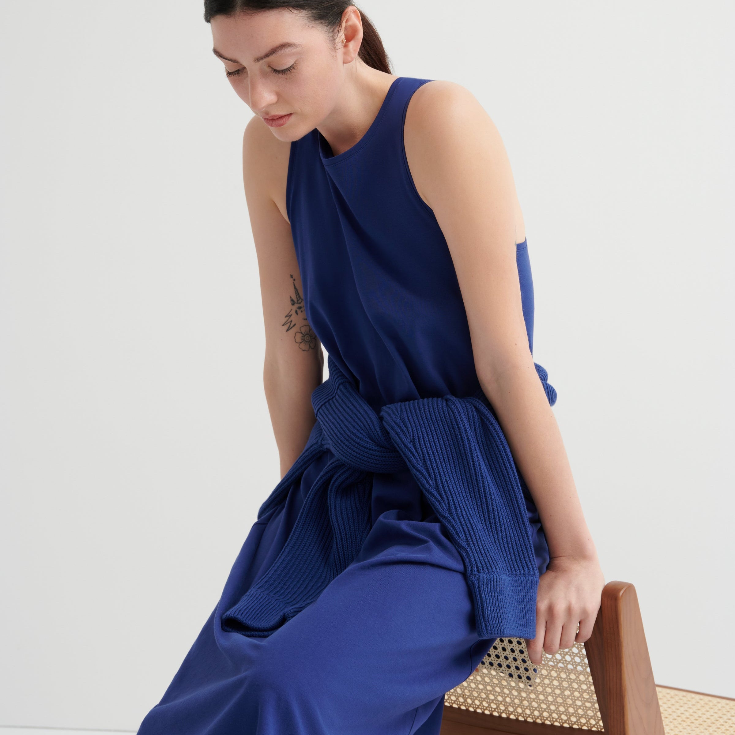 Woman wearing a blue dress sitting on a wooden chair against a white background