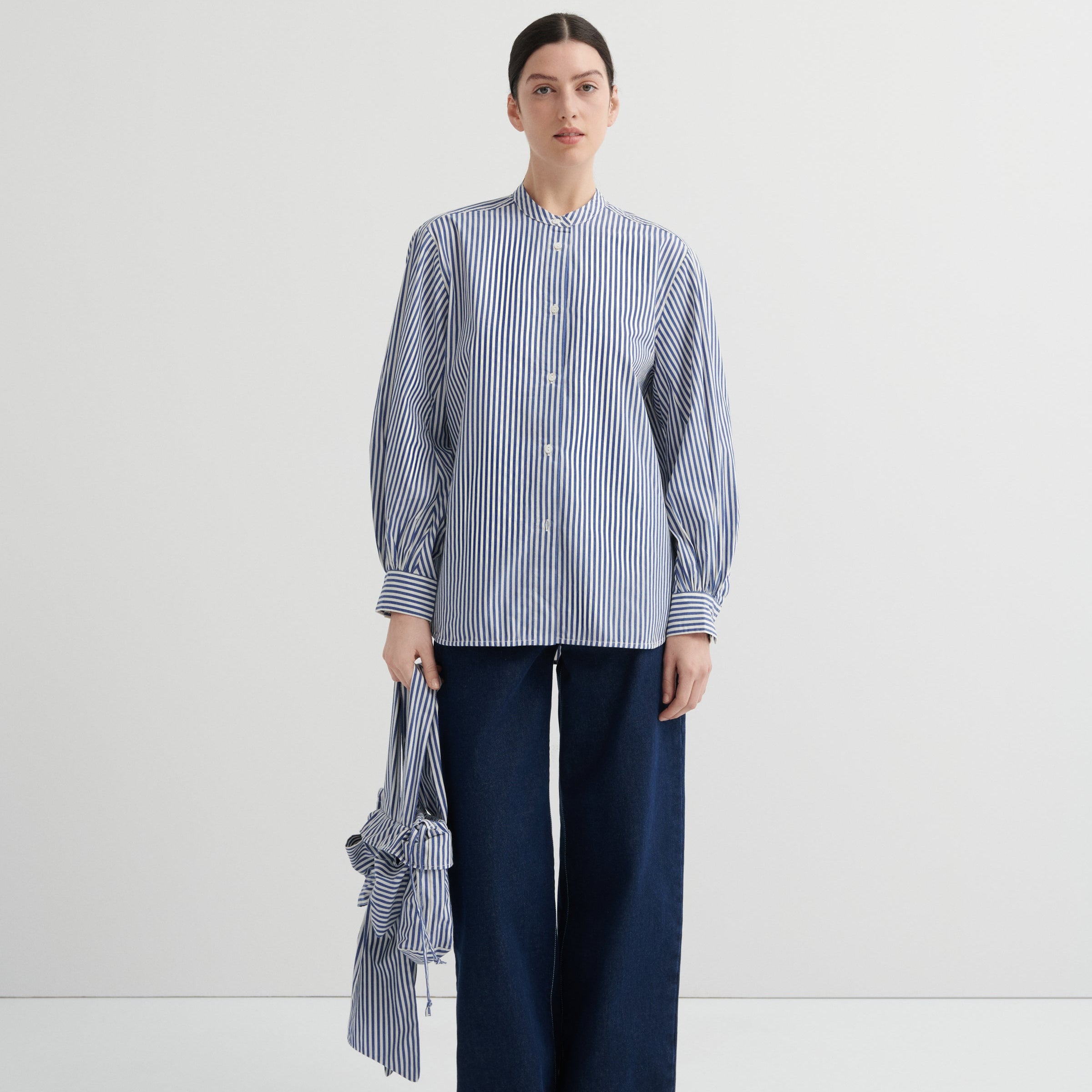 Person wearing a blue and white striped shirt with a long tie and dark pants on a white background