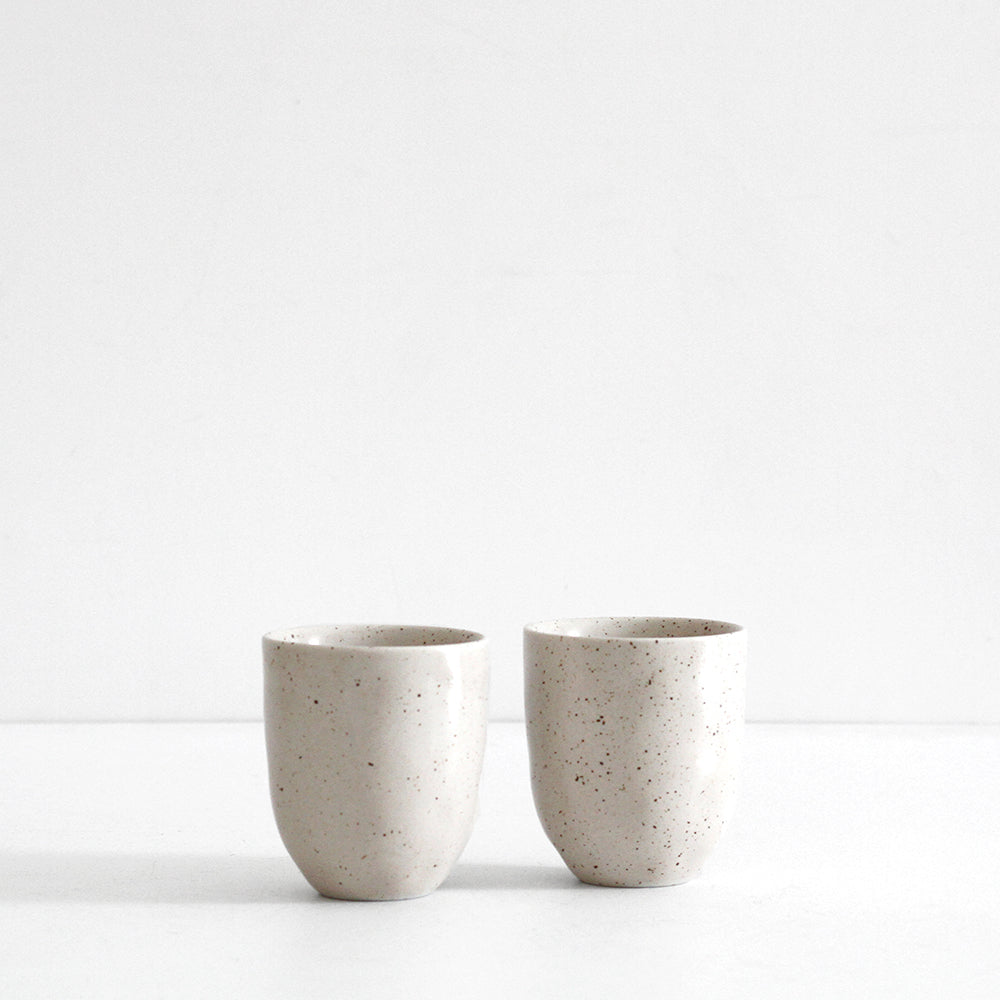 Two beige high-fired porcelain latte mugs on a white surface, viewed from the side.