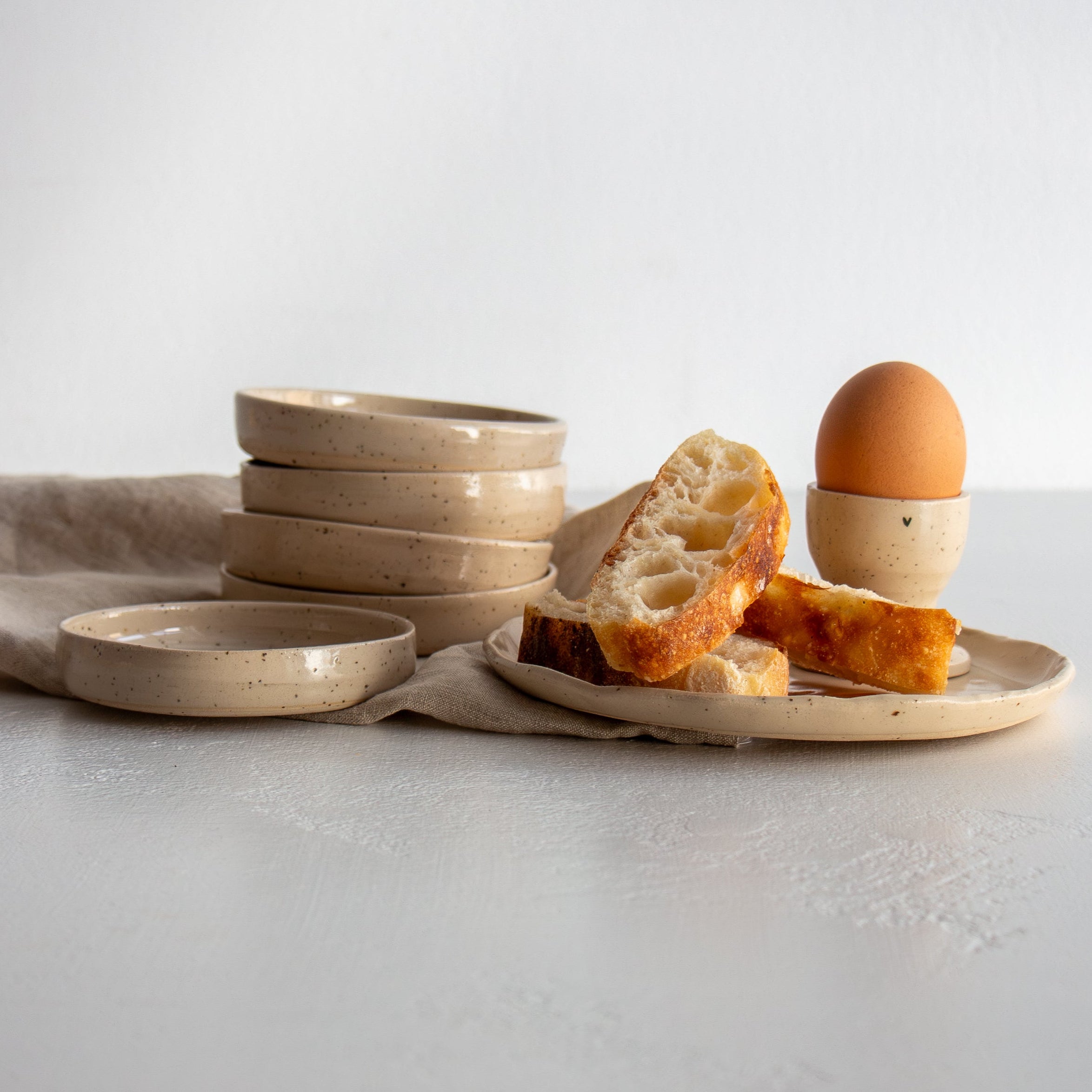 Set of ceramic bowls on a light surface with bread slices and ceramic egg cup
