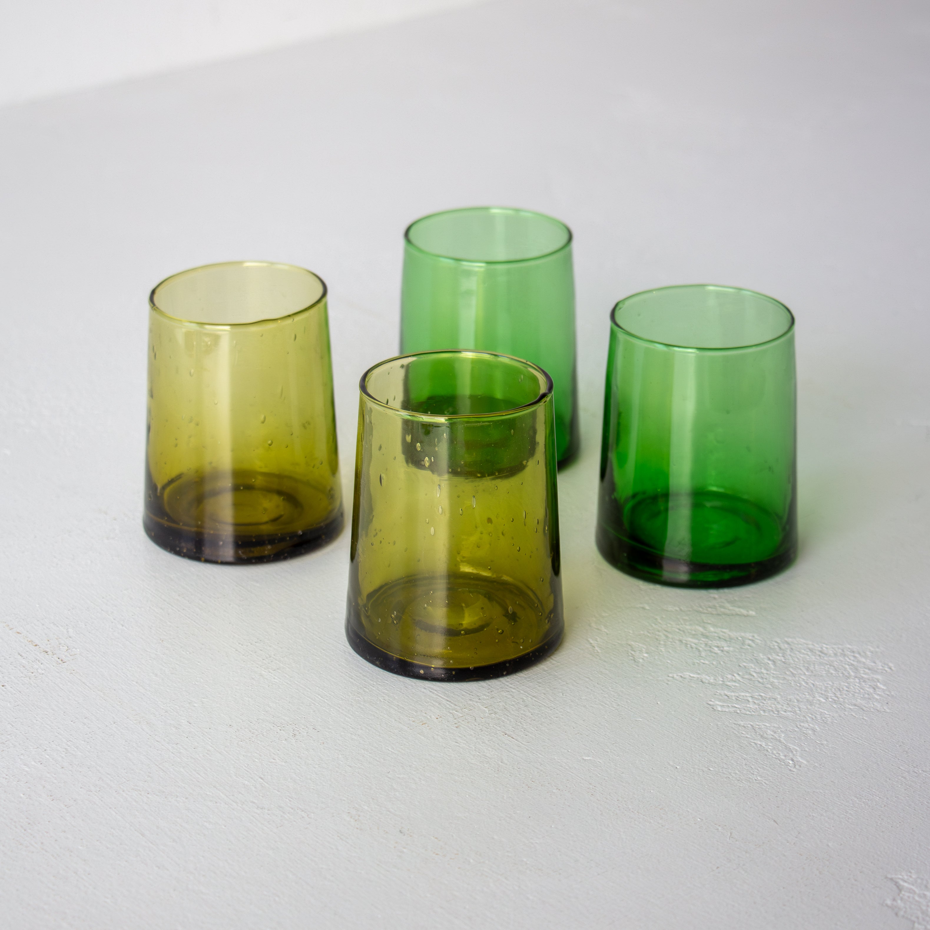Four green glass tumblers on a white surface