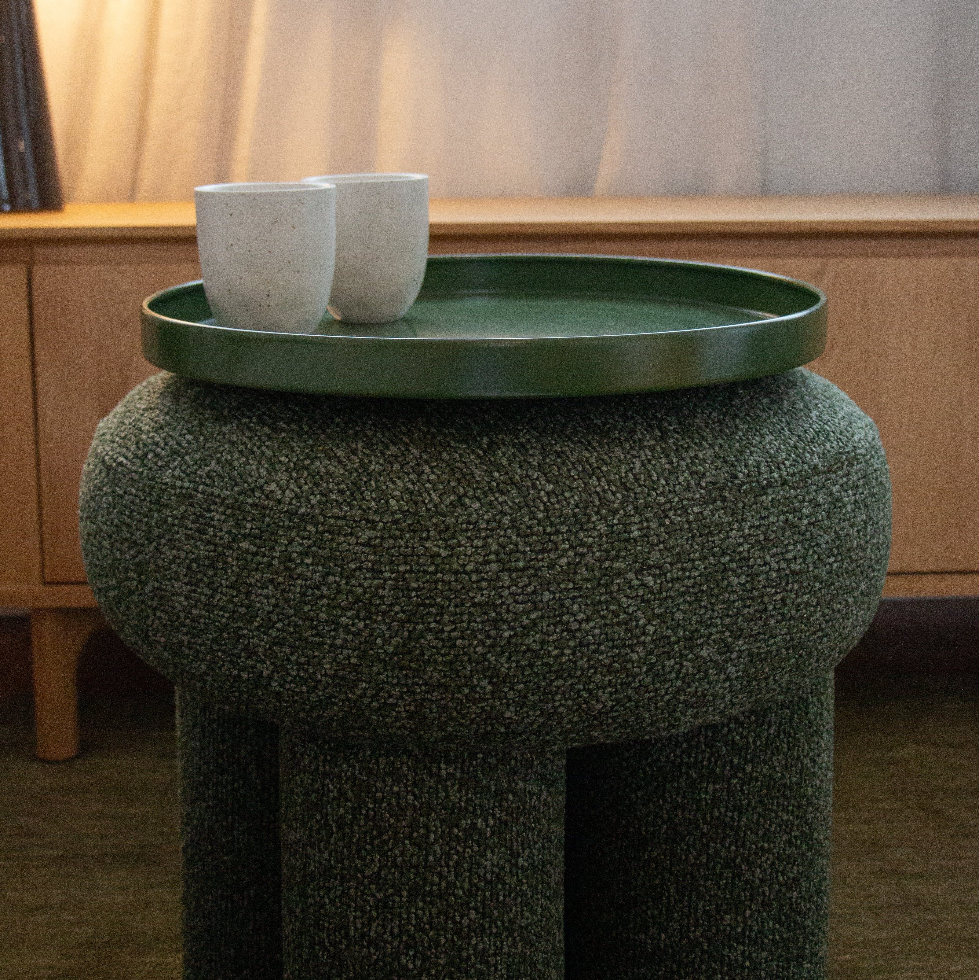 Green textured stool with a round green tray holding two white cups on a wooden surface.