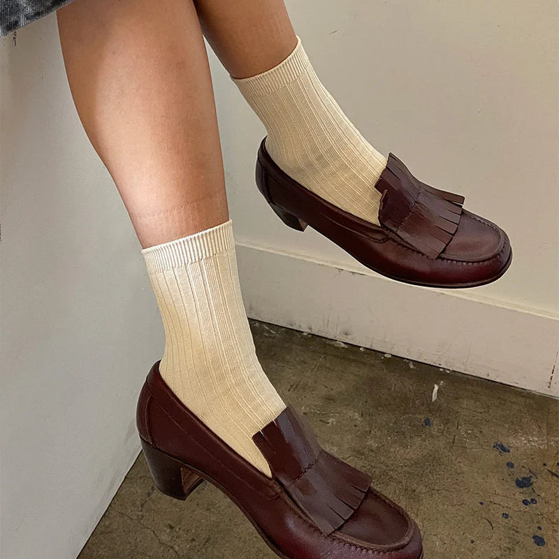 Person wearing brown loafers and beige socks against a neutral background