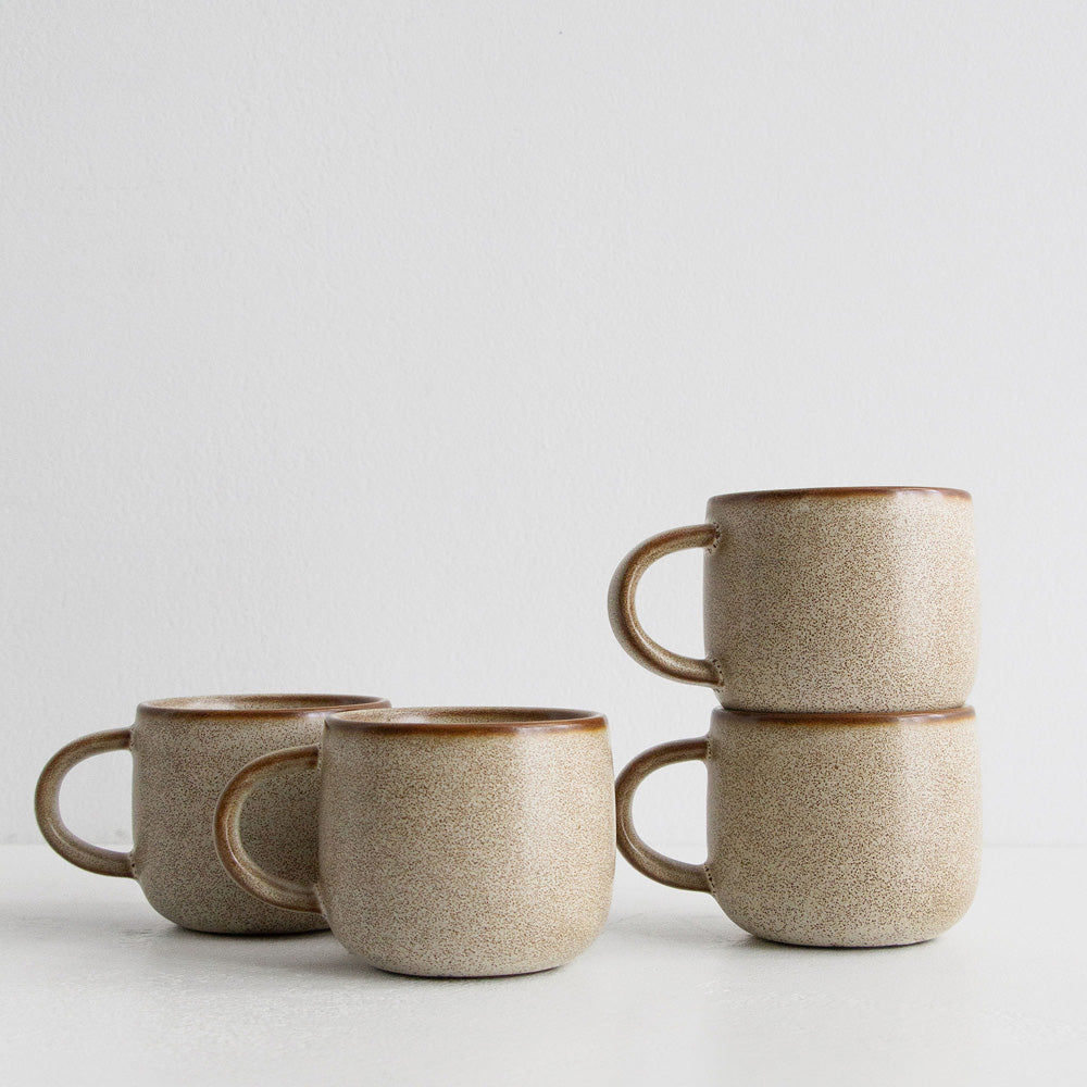 Set of four ceramic mugs with brown rims on a light gray background
