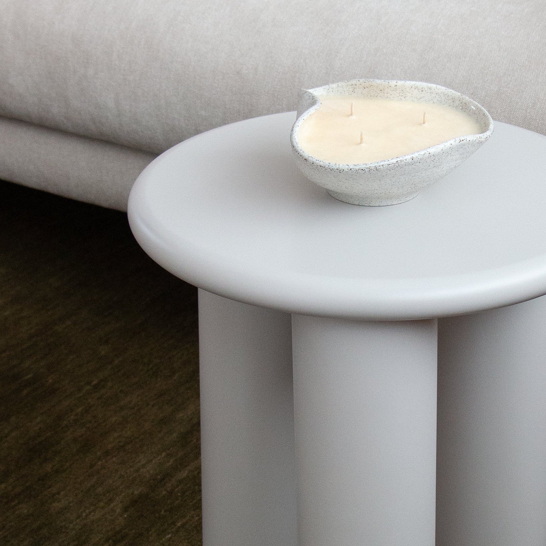 Modern cream side table with a candle on it next to a sofa